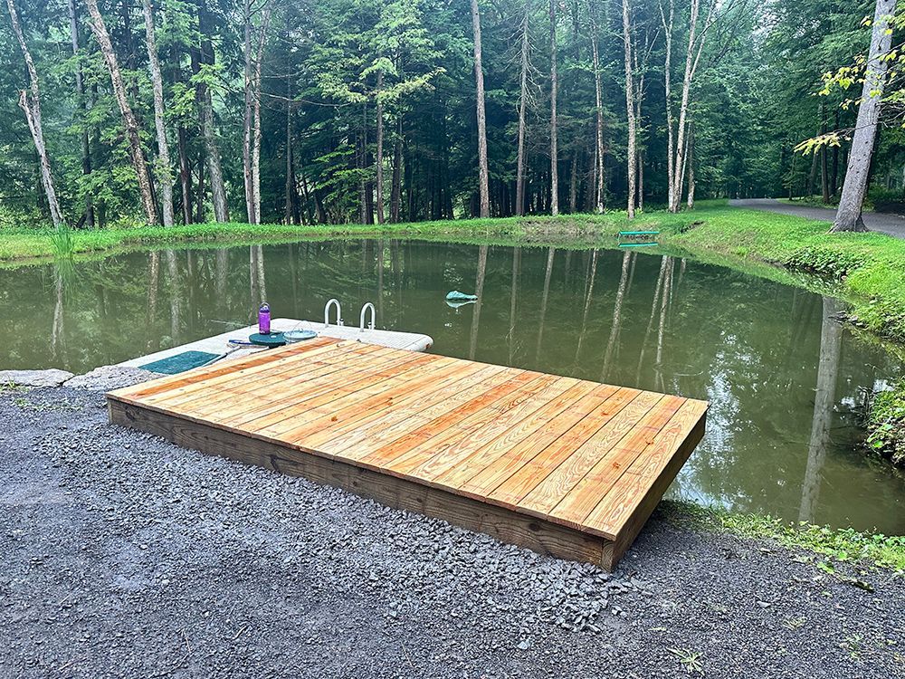 A wooden dock is sitting next to a pond surrounded by trees.