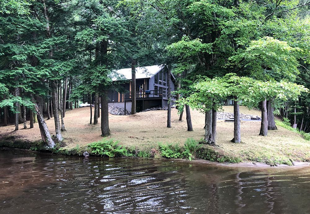 A house is sitting on a small island in the middle of a lake surrounded by trees.