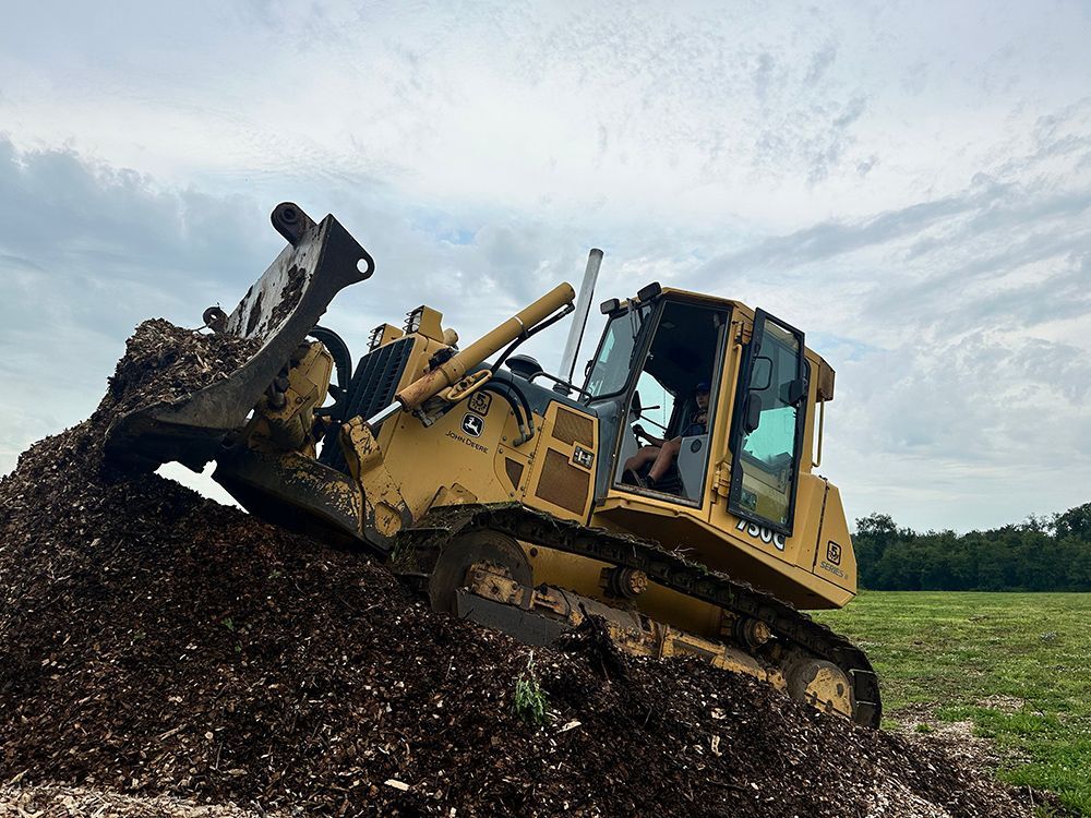 A bulldozer is moving a pile of dirt in a field.