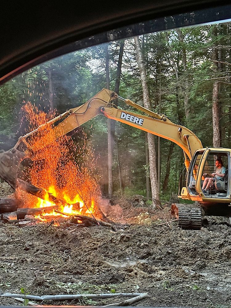A deere excavator is working on a fire in the woods.
