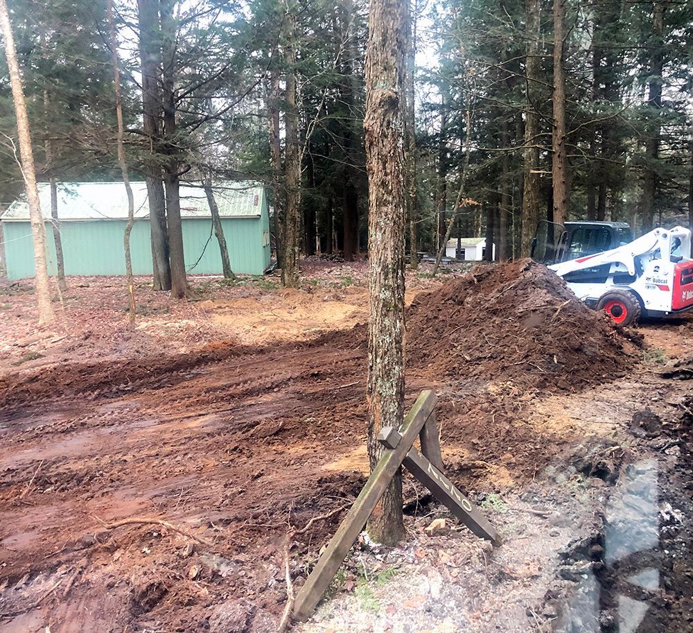 A bulldozer is driving through a dirt field in the woods.
