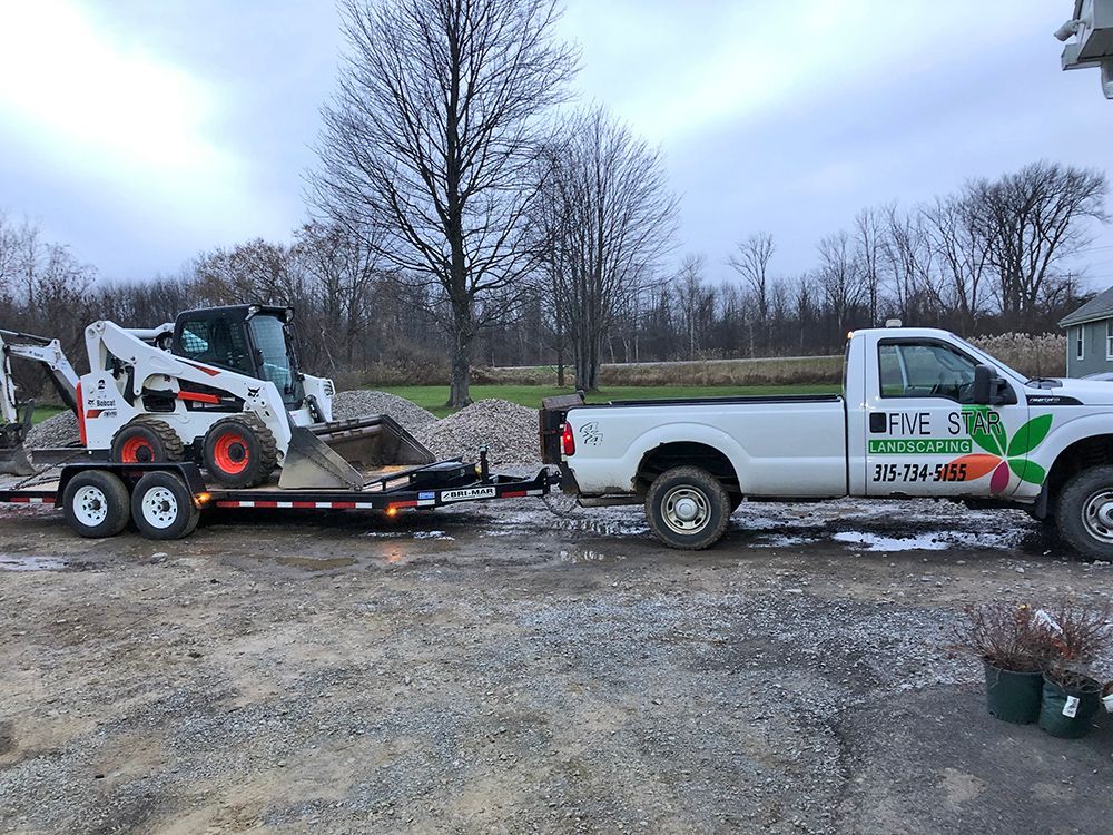 A white truck is towing a bobcat on a trailer.