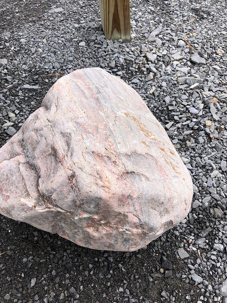 A large rock is sitting on the ground next to a wooden post.