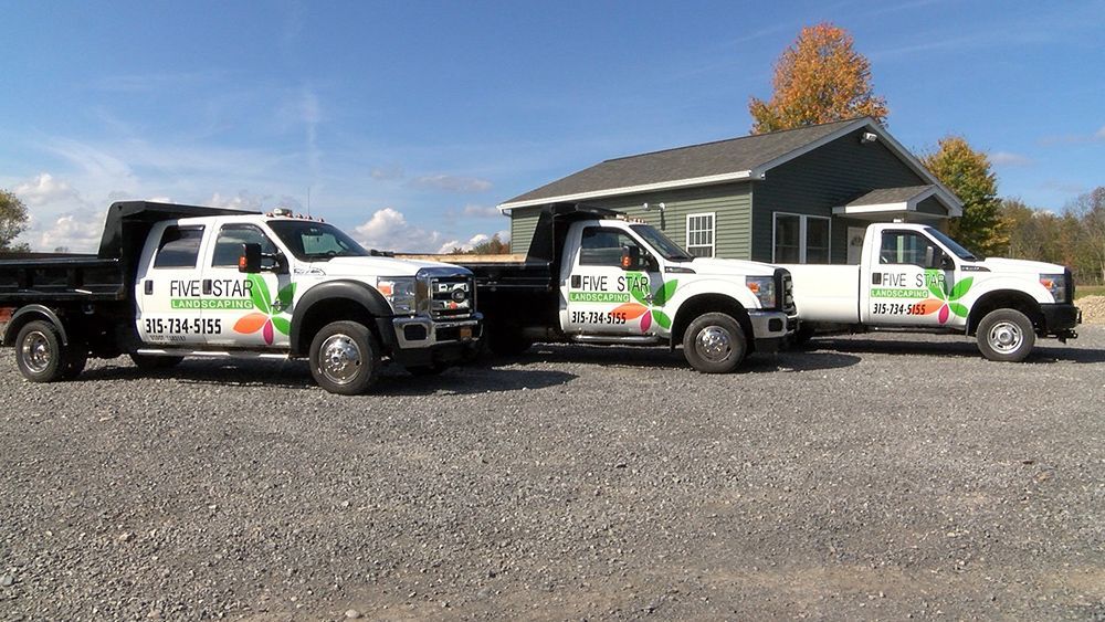 Three trucks are parked in a gravel lot in front of a house.