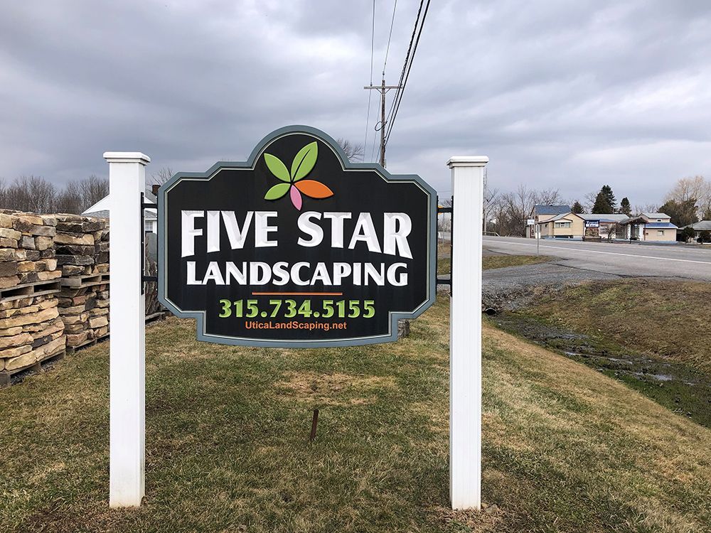 A sign for five star landscaping is sitting in the grass.
