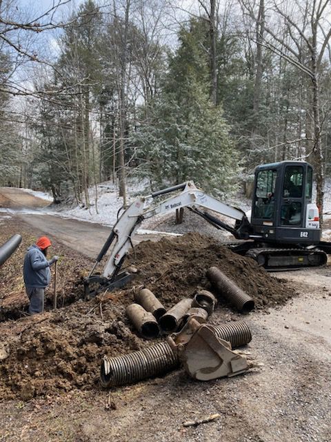 A man is standing next to a pile of pipes next to an excavator.