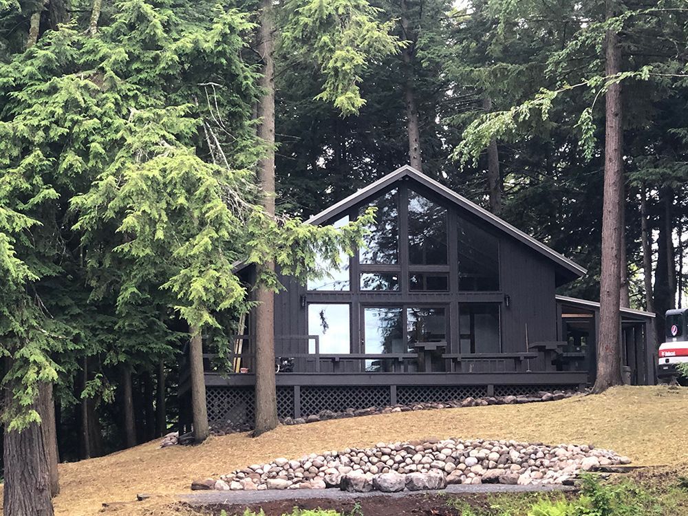A black house with a lot of windows is surrounded by trees.
