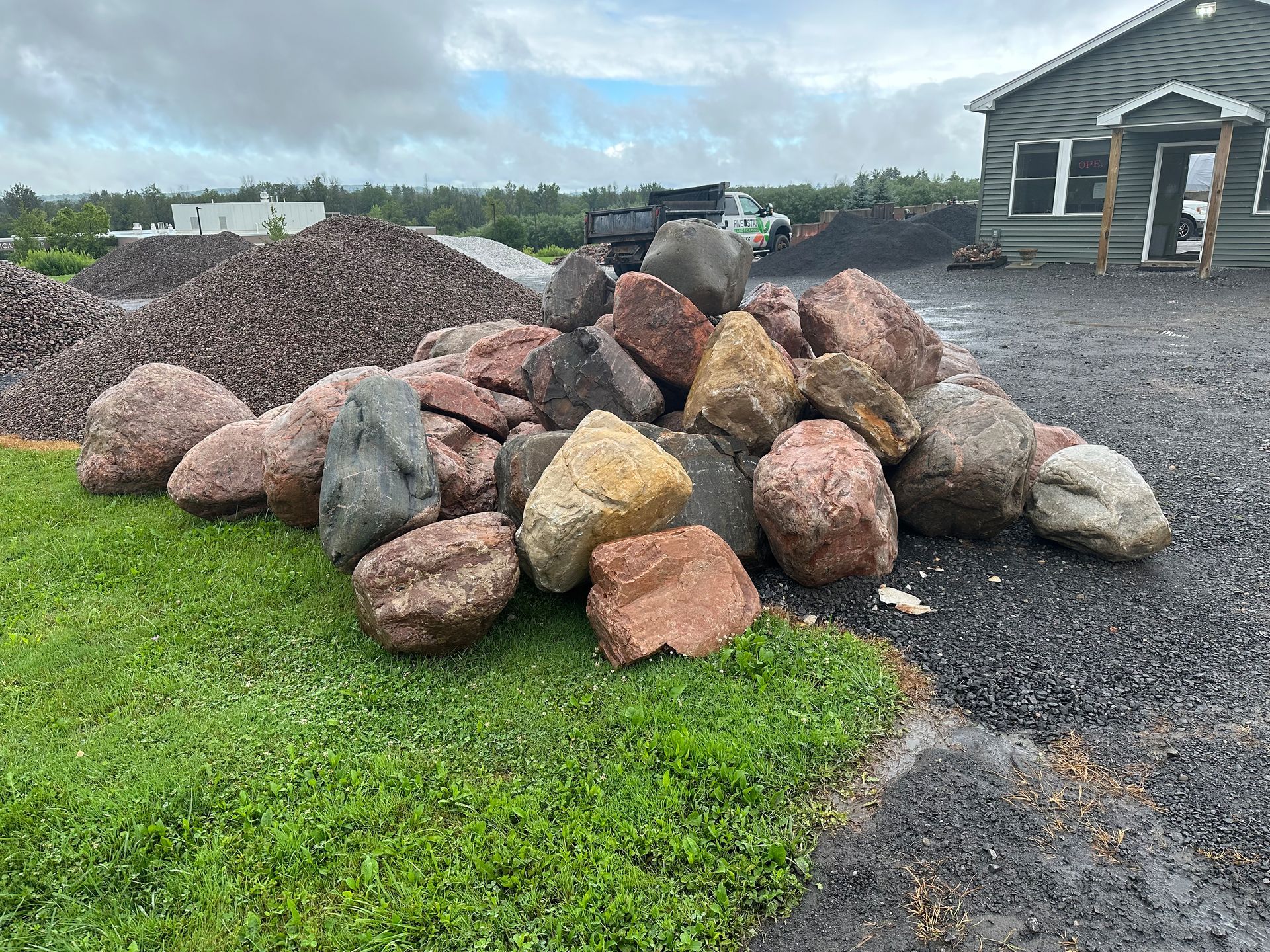 A pile of rocks is sitting in the grass in front of a house.