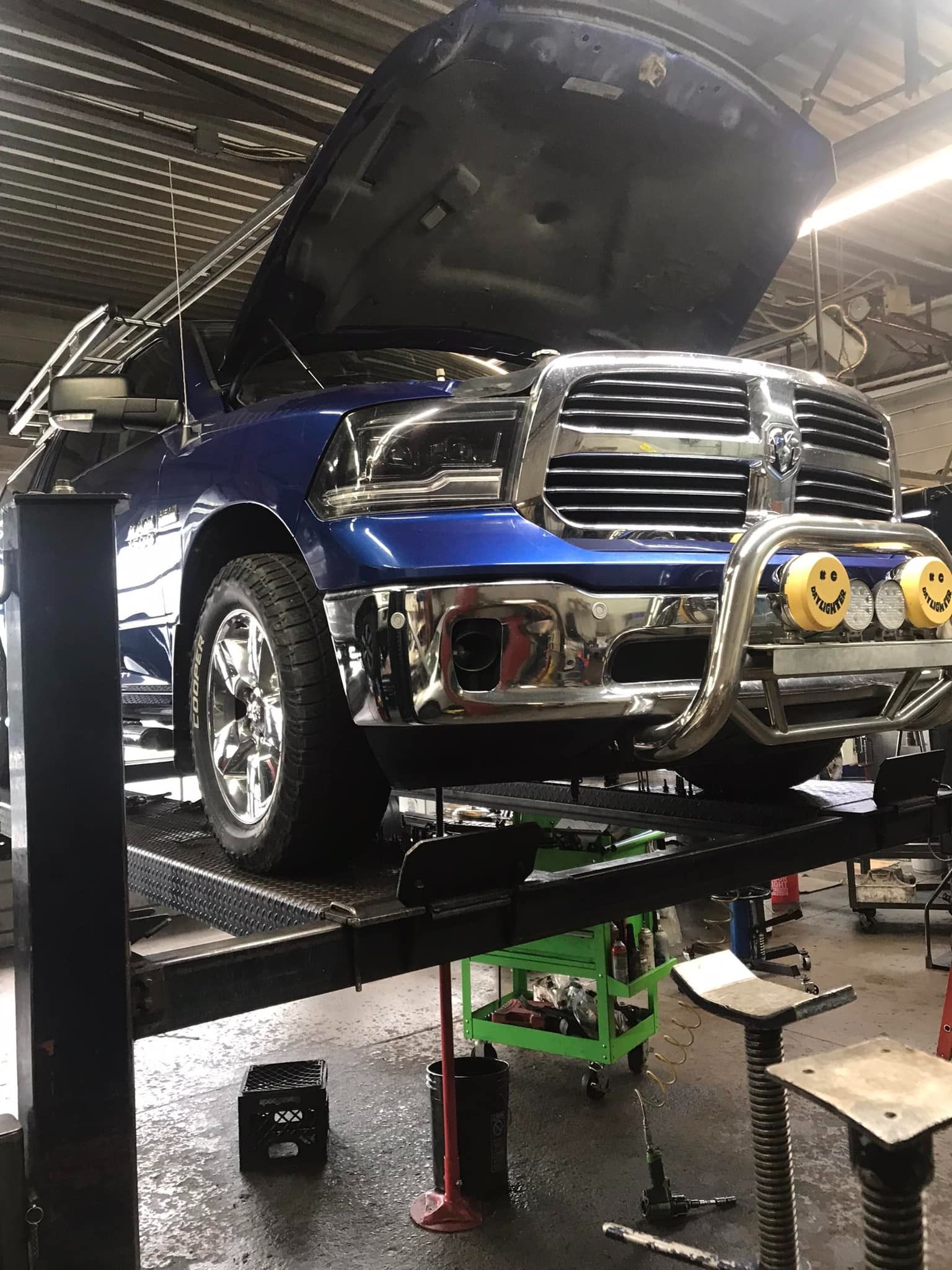 Blue Ram pickup truck on a lift in a repair shop, hood open.