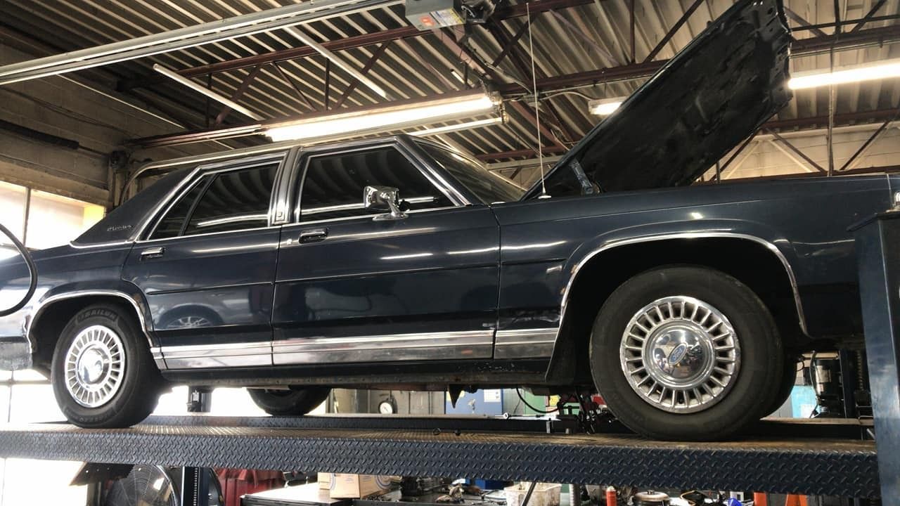 A dark blue sedan on a lift with its hood open inside a garage.