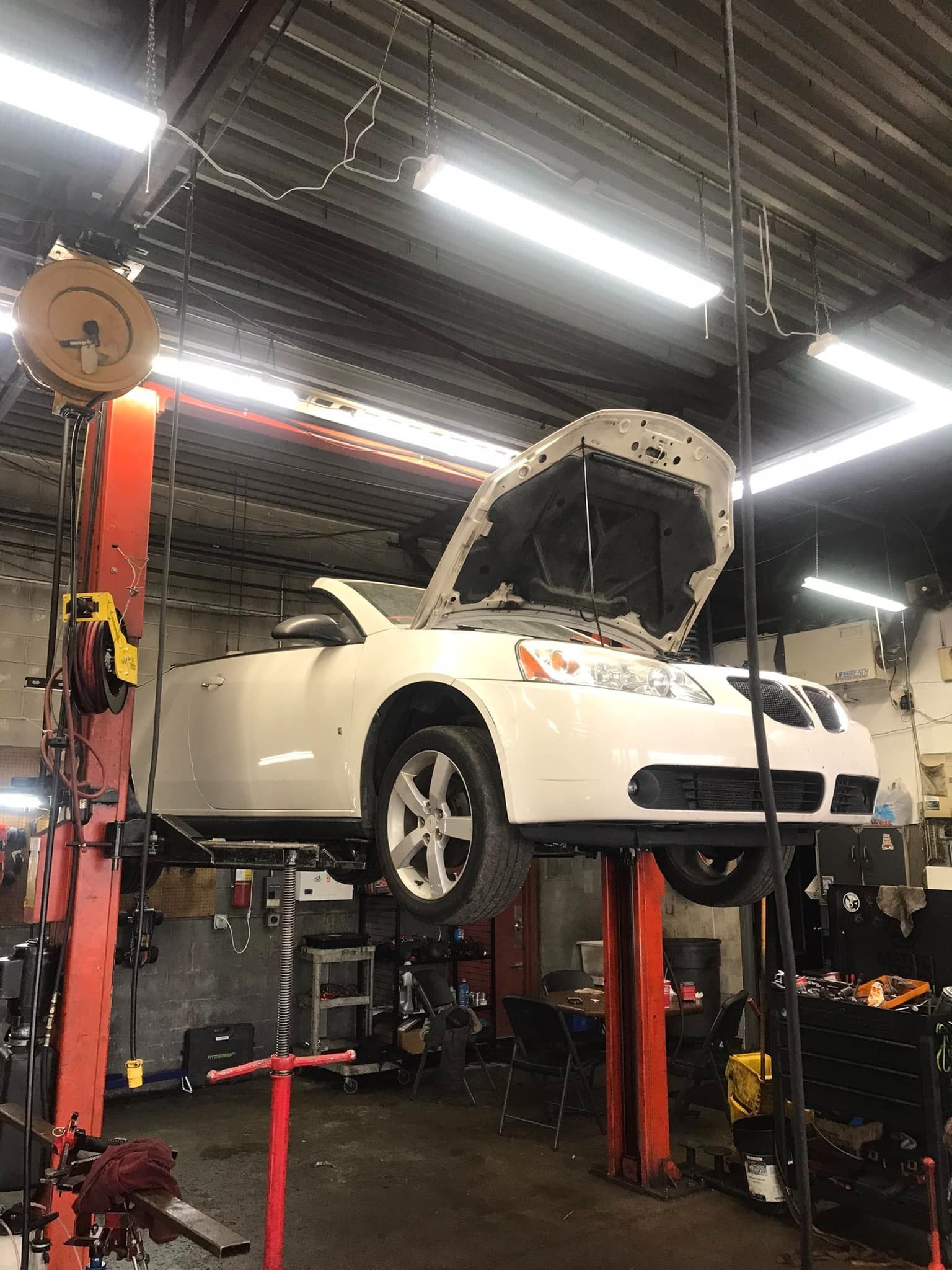 White car with open hood on a lift in a garage for repair.