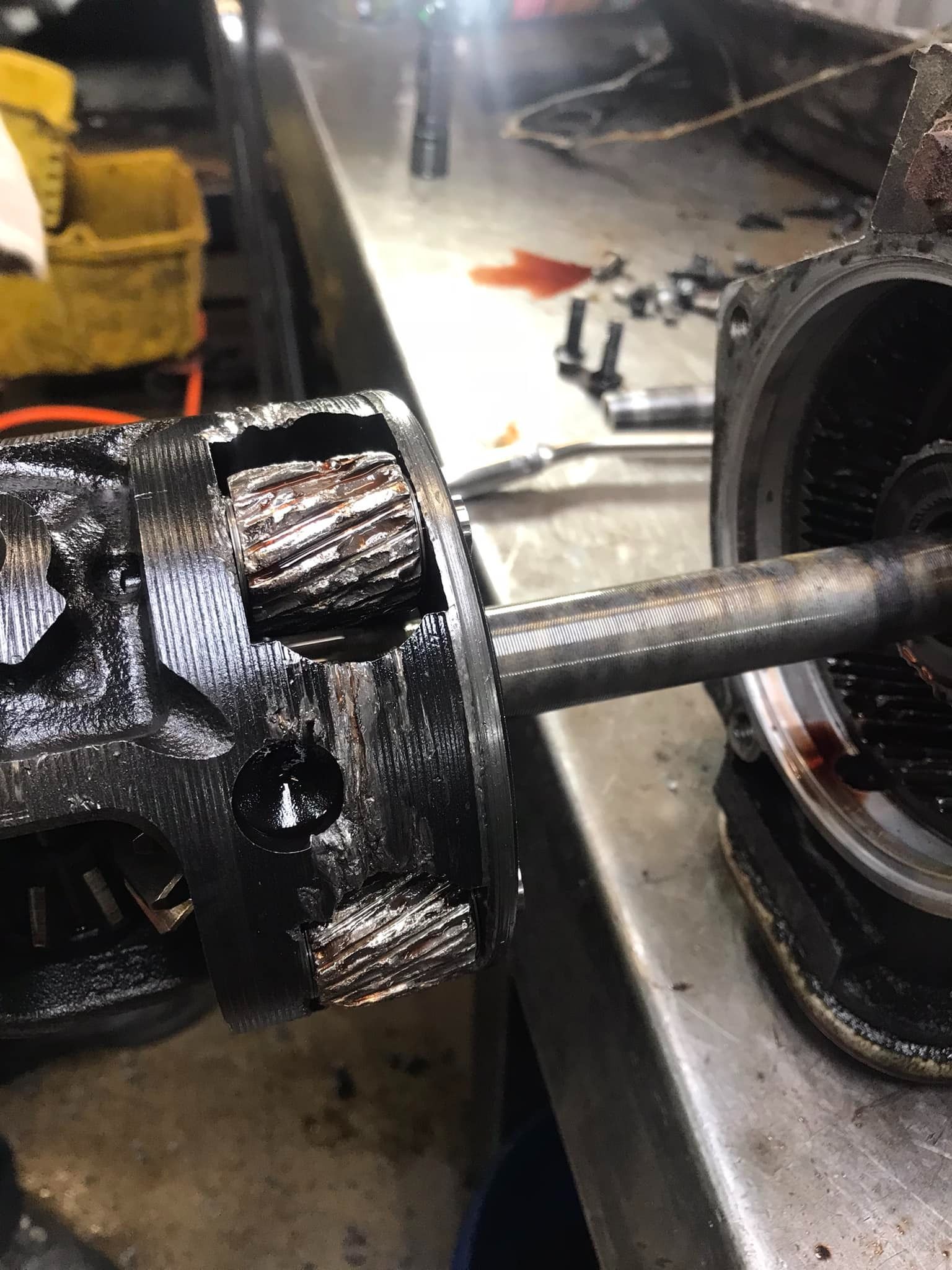 Damaged car part, covered in black grime, on a workbench. Close-up shows severely worn gears.