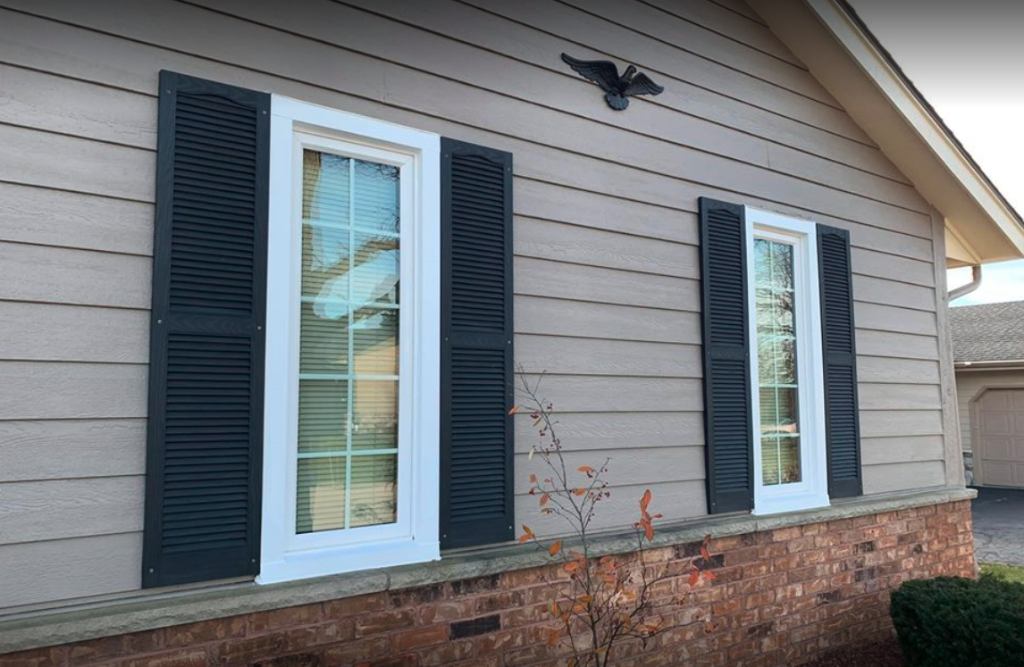 A house with black shutters on the windows and a bird on the roof.