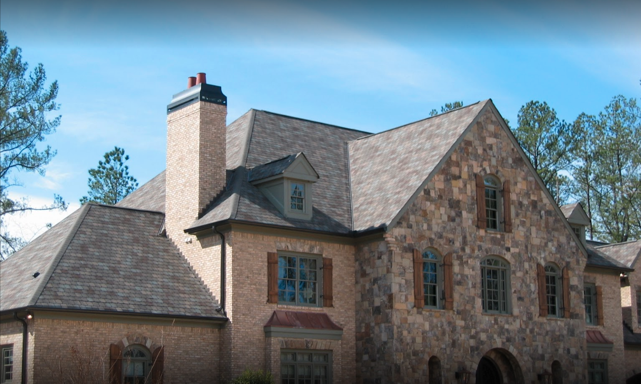A large stone house with a gray roof and a chimney.