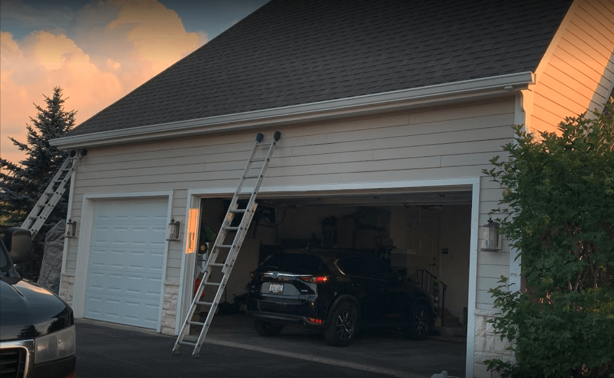 A car is parked in a garage with a ladder hanging from the roof.