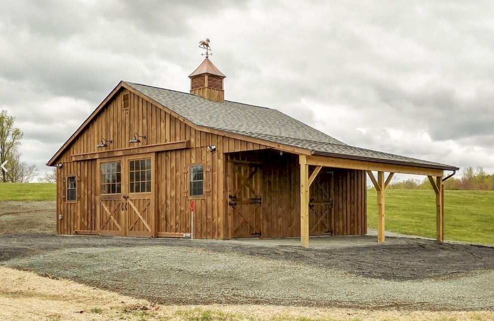 Rustic wooden barn with a small cupola on a gravel lot under a cloudy sky