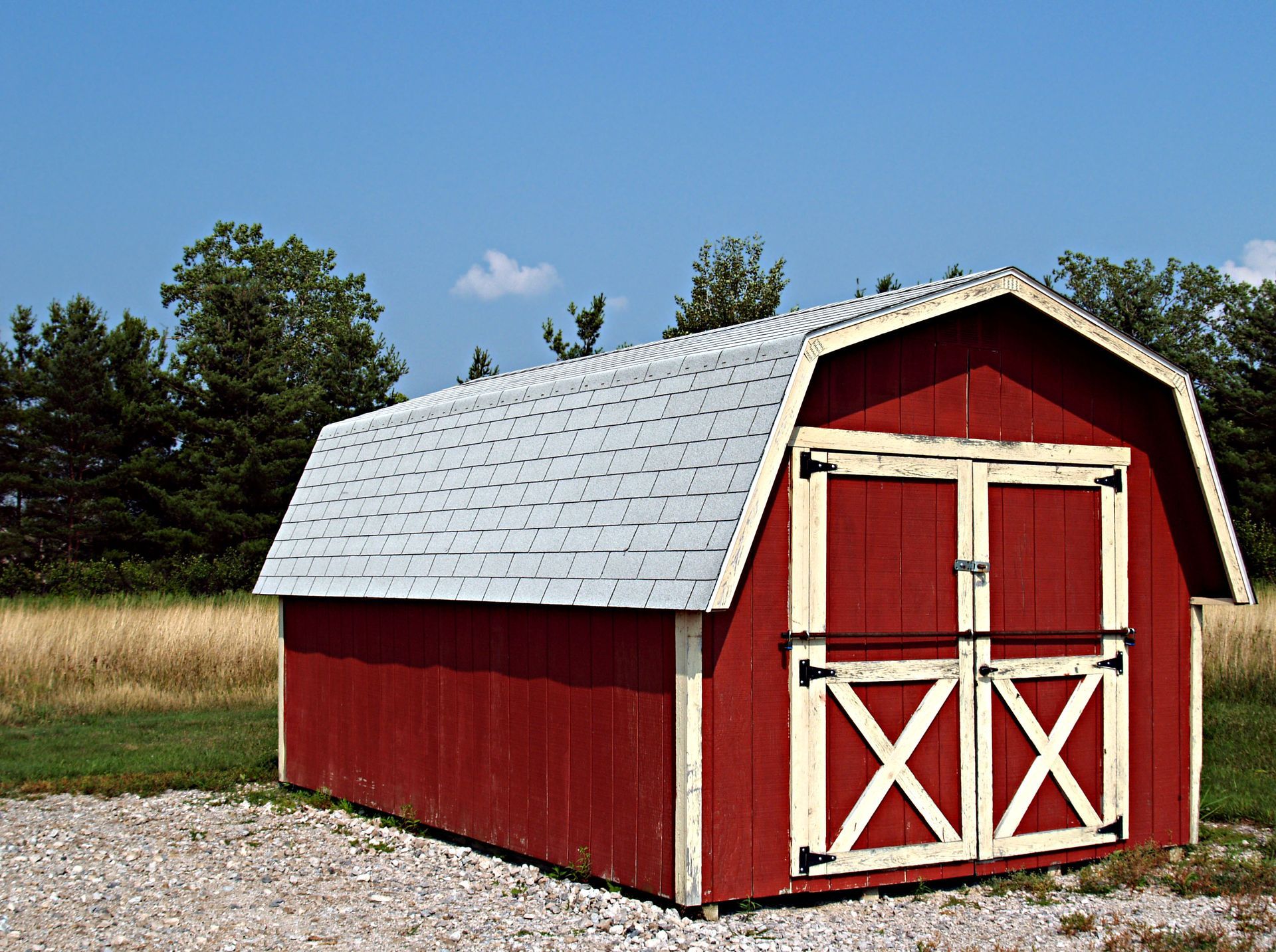 Red barn shed with white trim and doors on a gravel lot under a blue sky
