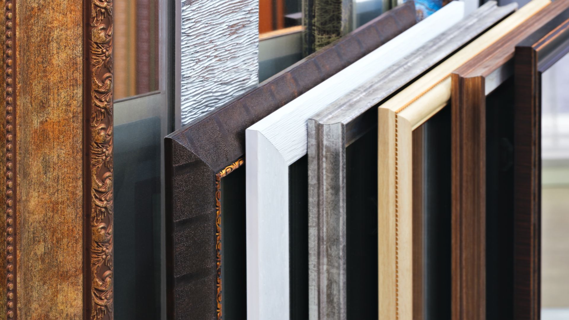 A row of varied picture frames in different materials, textures, and colors, including wood, white, and metallic finishes.