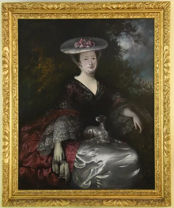 A woman in a wide-brimmed hat and ornate, dark-and-silver dress sits with a small dog on her lap in a landscape.