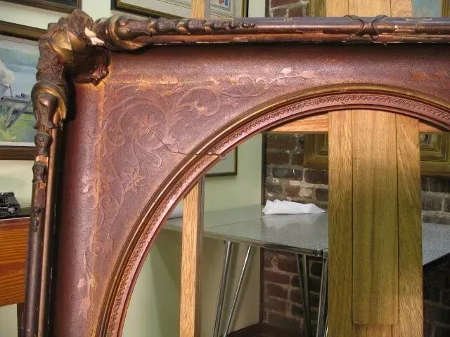 An ornate, dark wood picture frame with carved floral details on a wooden easel in an art studio.
