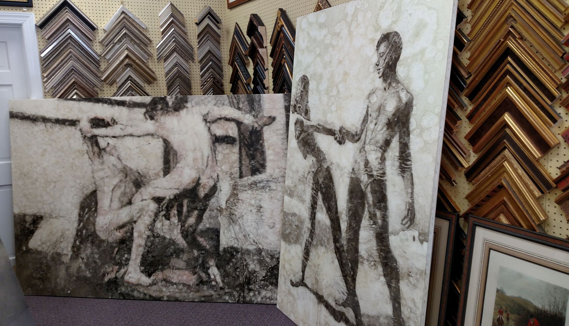 Art store display with black-and-white figurative paintings and stacks of ornate picture frames.