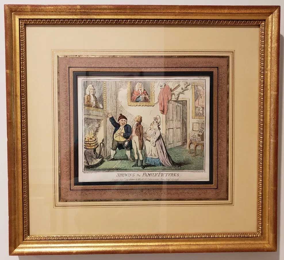 A framed, satirical 18th-century hand-colored print showing three figures in a room with portraits on the wall.