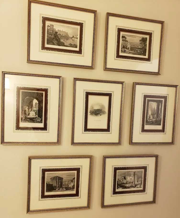A gallery wall displaying seven framed black-and-white landscape prints arranged in three rows against a cream wall.