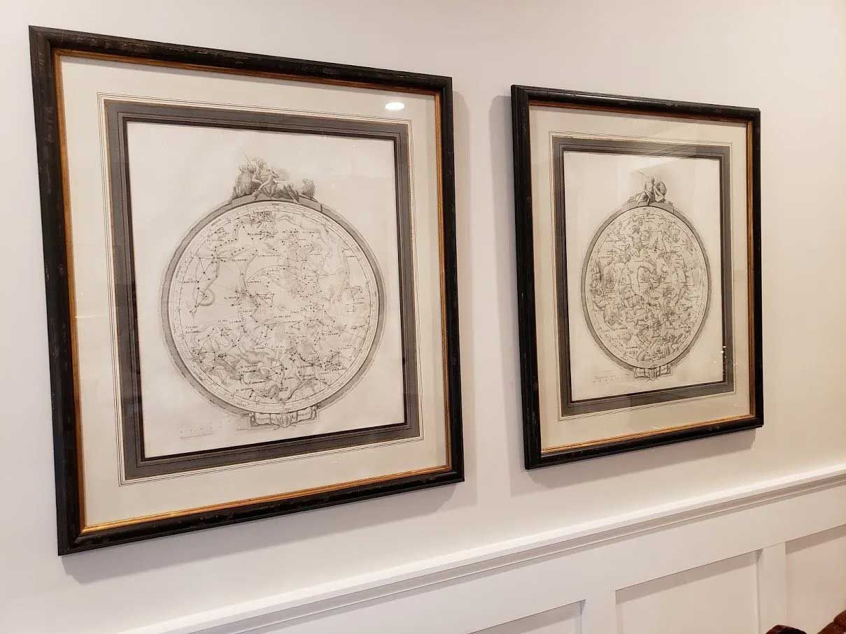 Two framed, circular, monochromatic illustrations of detailed maps hanging side-by-side on a white paneled wall.