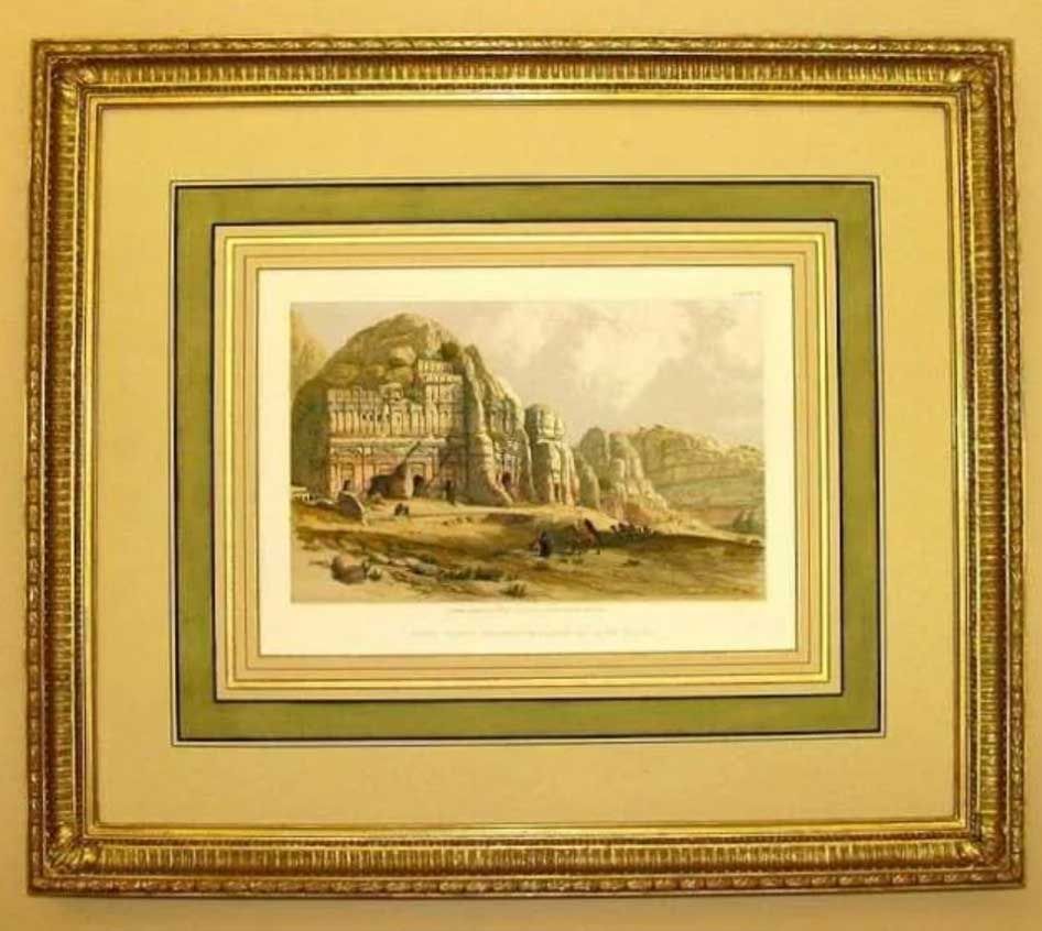 A framed, sepia-toned print depicting an ancient stone cliff dwelling or tomb carved into a craggy, desert landscape.