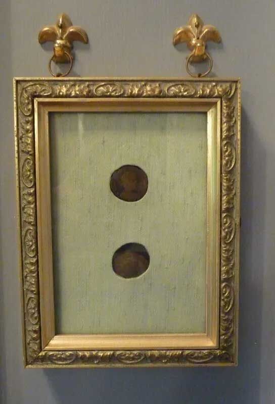 An ornate gold frame with a light green mat containing two circular cutouts, mounted to a wall with two fleur-de-lis.