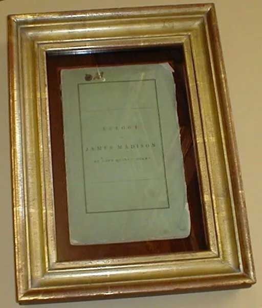 A framed, light green document titled with the name James Madison, displayed against a light-colored wall.