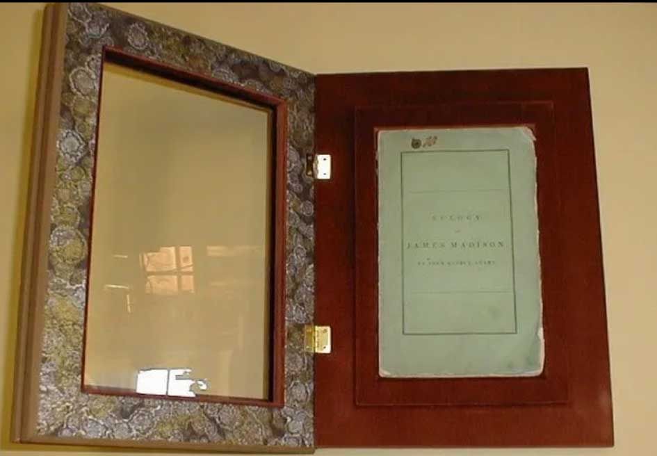 A light blue document is displayed inside a wooden hinged case with an ornate, patterned border on the glass-covered side.