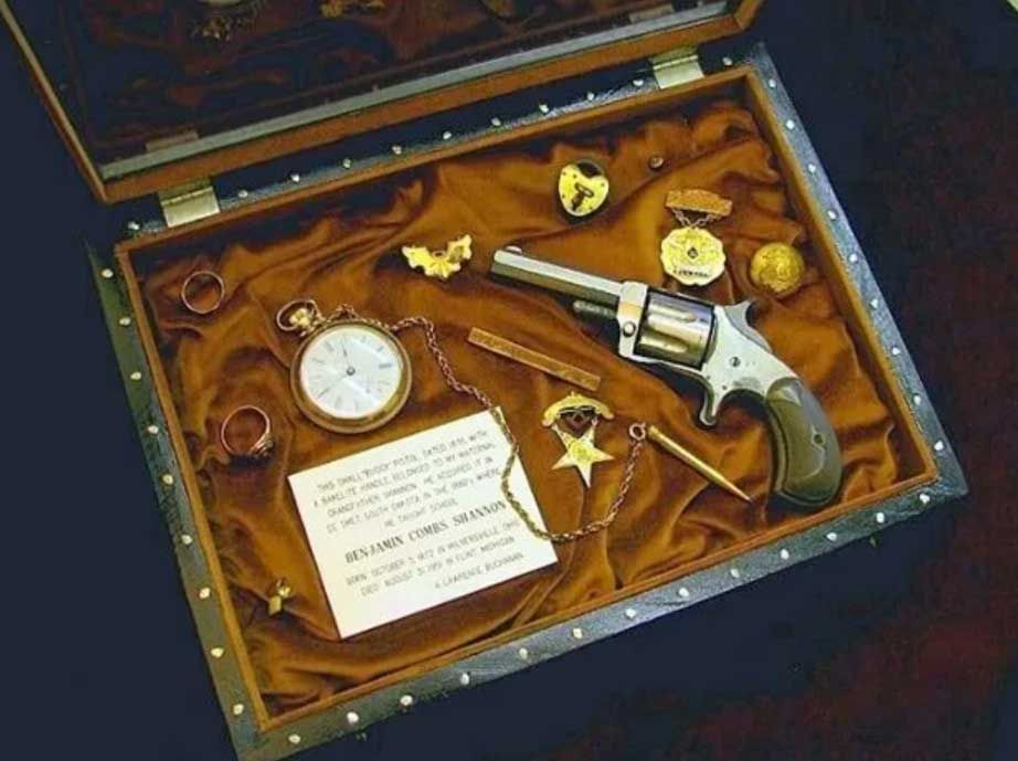 A velvet-lined box displays an antique pocket watch, a revolver, a star-shaped badge, and a commemorative card.