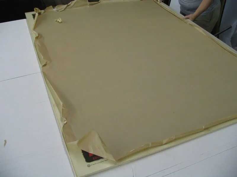 A large piece of cardboard or paper partially peeled back from the adhesive surface of a framed backing board.