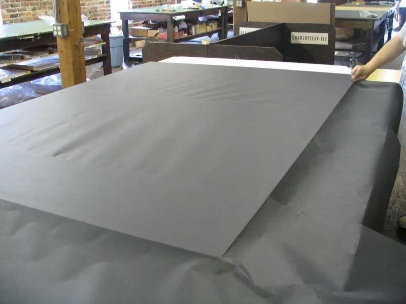 A hand positions a large, matte-grey sheet of material onto a black-covered work table in a studio setting.