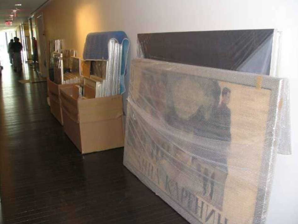 Cardboard boxes and a large, plastic-wrapped painting leaning against a hallway wall.