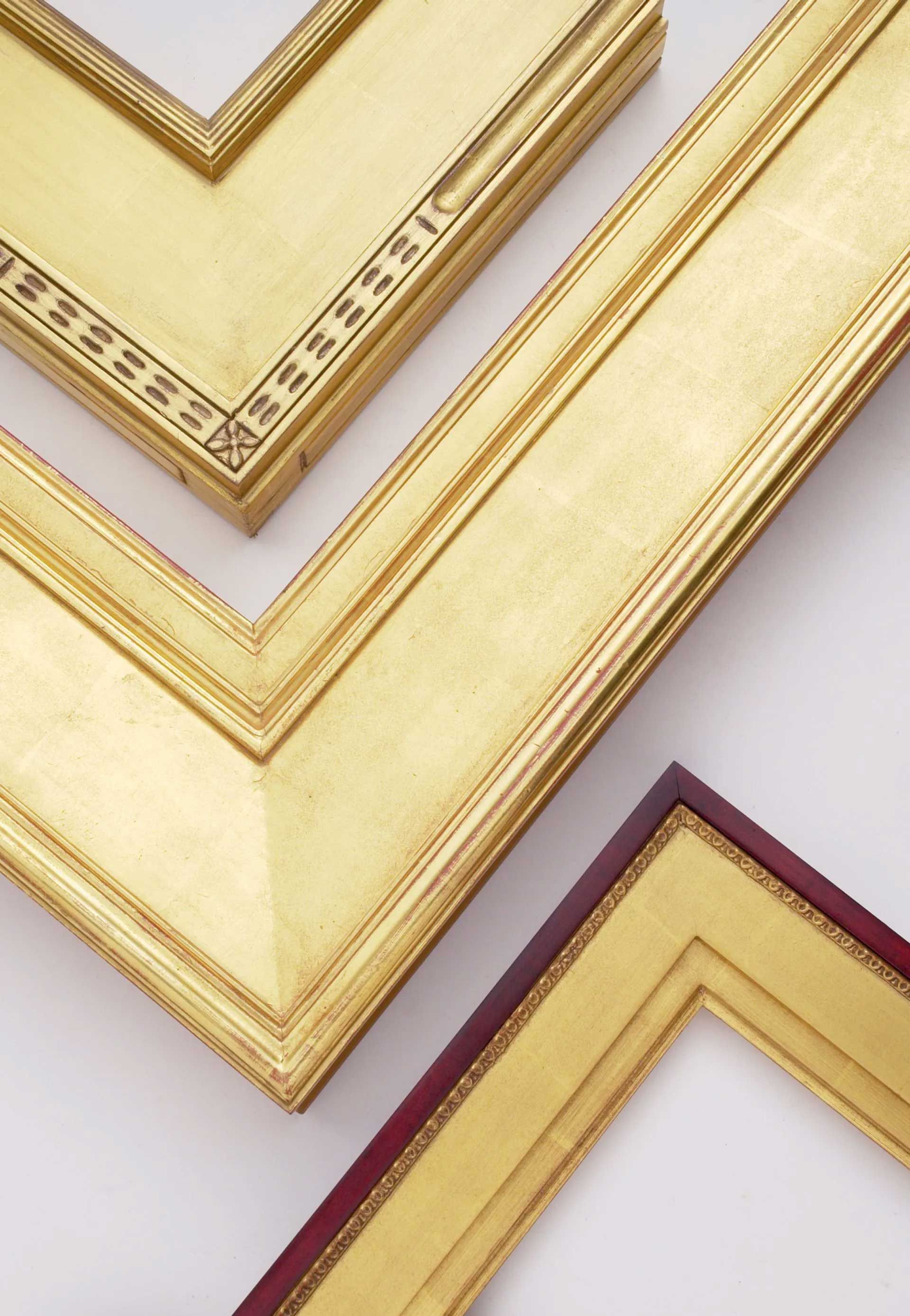 Three ornate, gold-finished picture frame corners are layered on a white background, showing different decorative motifs.
