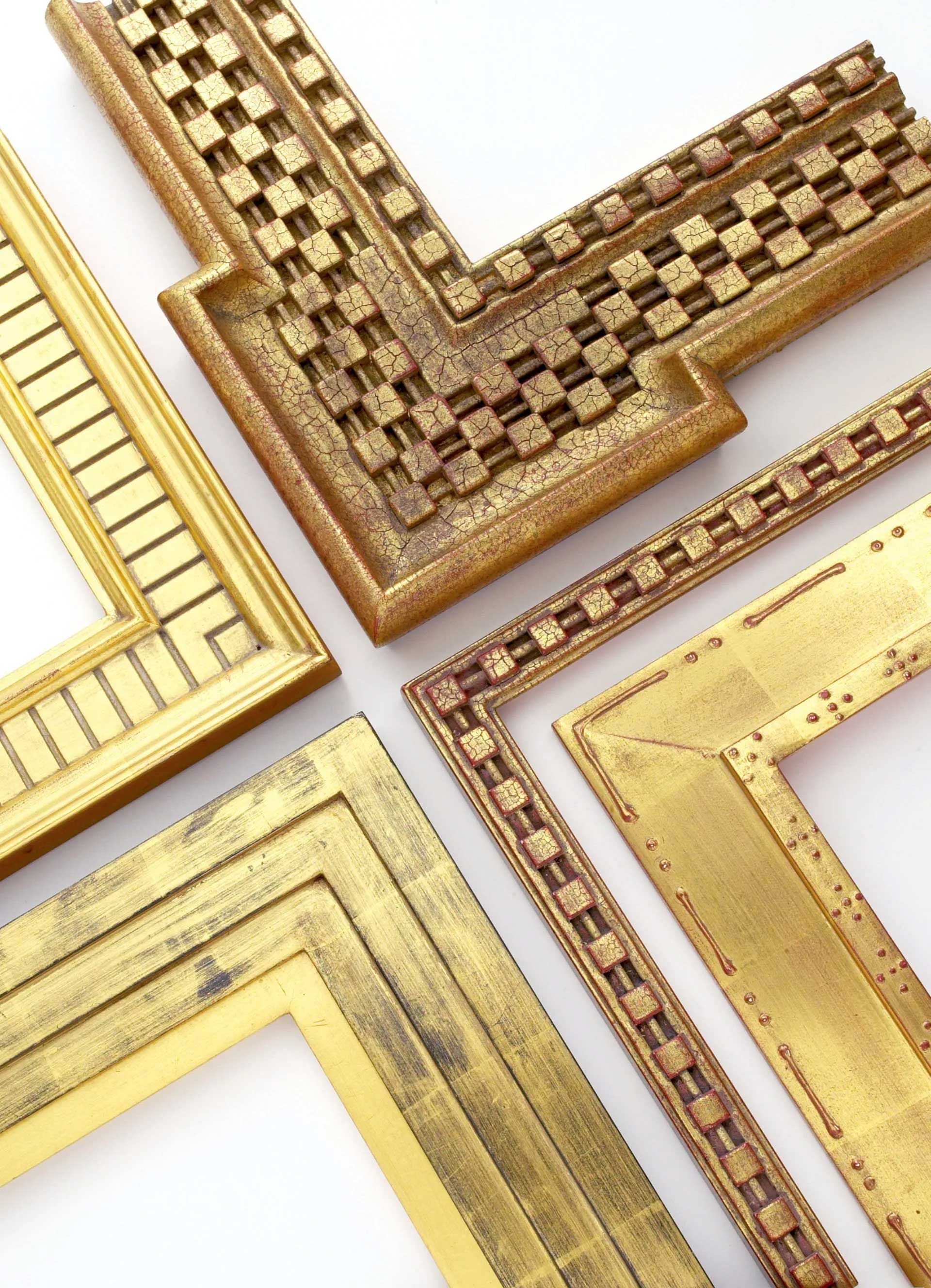 Four ornate, gold-colored picture frame corners with distinct textures and geometric patterns arranged on a white surface.