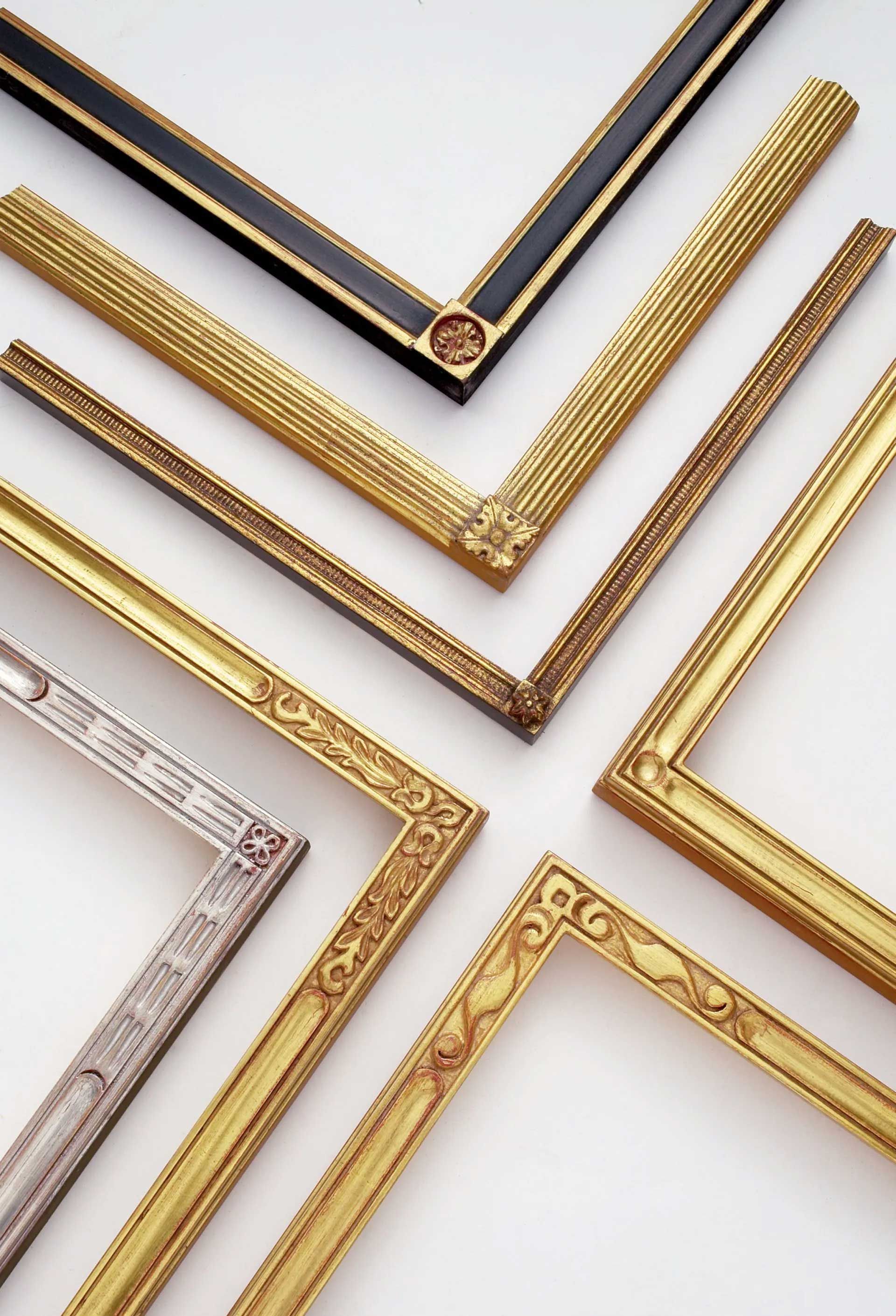 Several ornate picture frame corners in various metallic gold and silver styles are arranged on a white background.