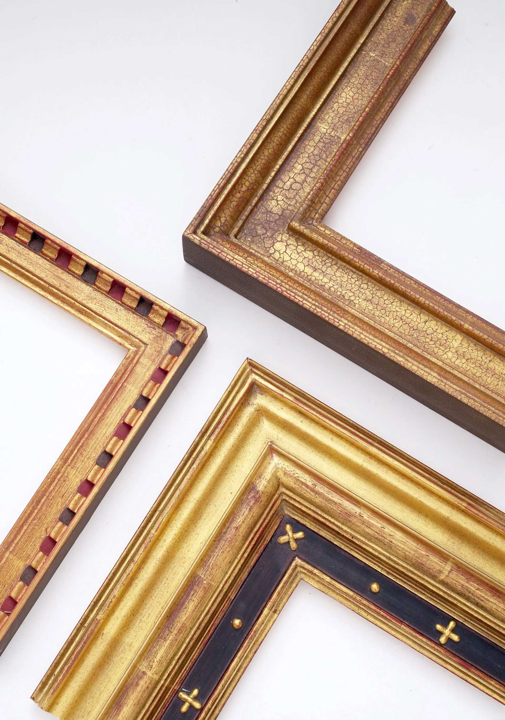 Three ornate, gold-toned picture frame corners with distinct textures and patterns arranged against a white background.