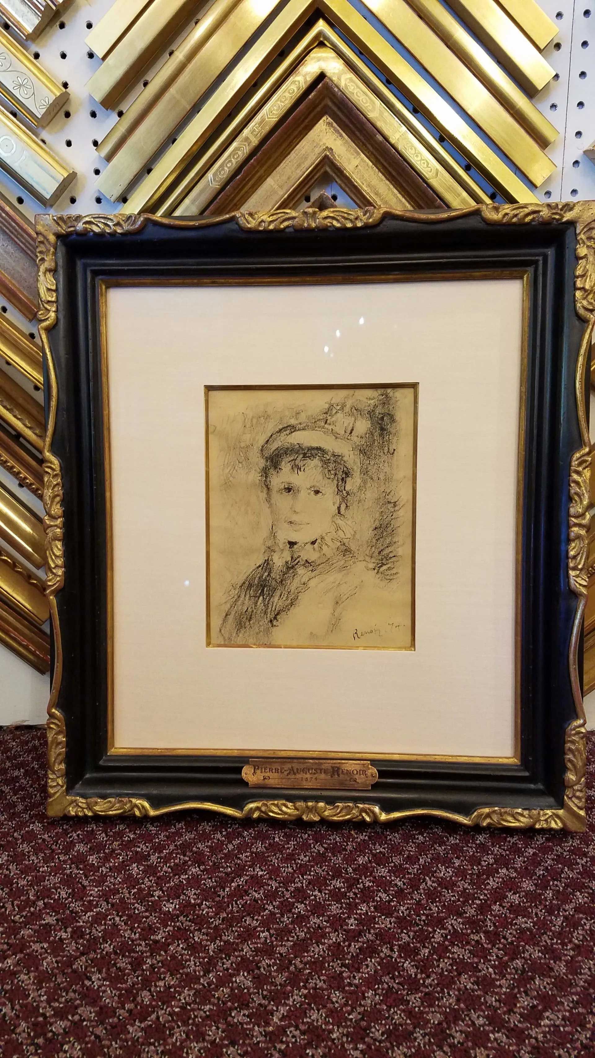 A framed, sketched portrait of a person in a decorative gold and black frame, set against a background of molding samples.