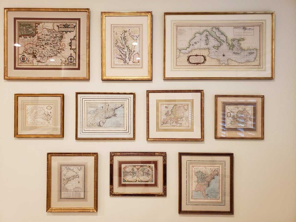 A gallery wall displaying ten framed antique maps in various sizes with gold and dark wood frames on a plain white wall.