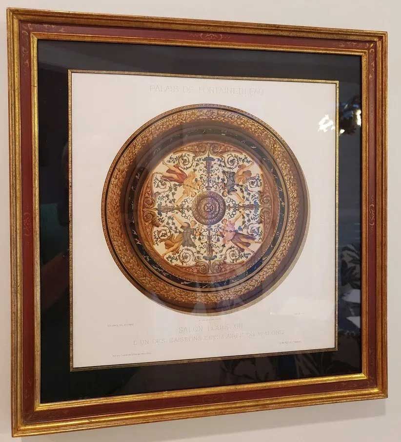 A framed print of a circular, ornate decorative plate featuring intricate floral patterns and figures in a red-gold frame.