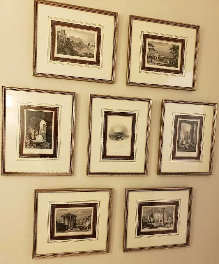 A wall gallery with seven framed black and white landscape prints arranged in three rows against a cream-colored wall.