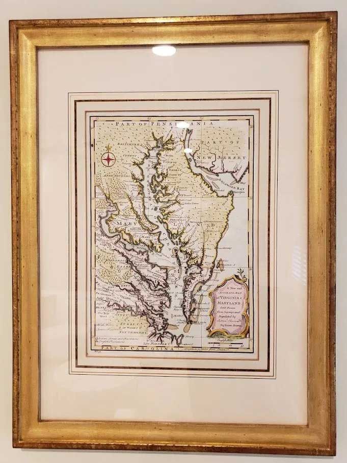 An antique, hand-colored map of the Chesapeake Bay region, framed in a gold-toned wooden frame hanging on a wall.