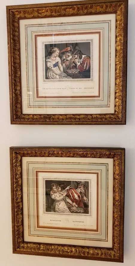 Two framed classical etchings in ornate gold frames, stacked vertically on a white wall.