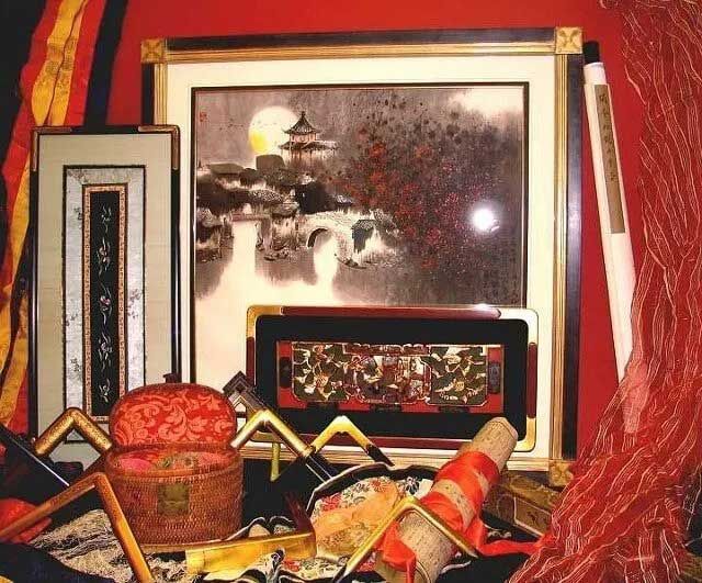 A collection of framed Asian-style artwork, a decorative box, and red fabric textiles arranged against a red background.