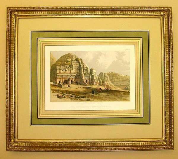 A framed, vintage-style print depicting ancient carved rock structures in a desert landscape with small human figures.