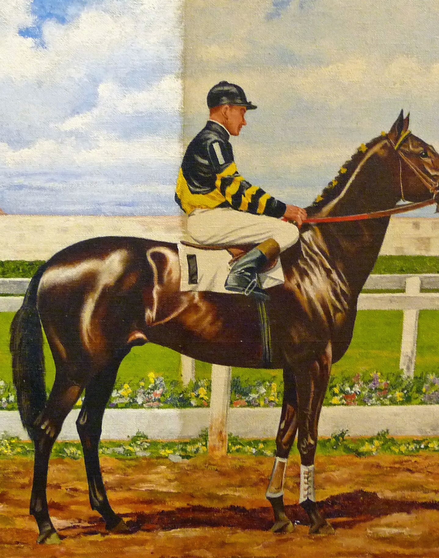 Jockey on a dark horse standing in a paddock, with a blue sky and white fence behind.