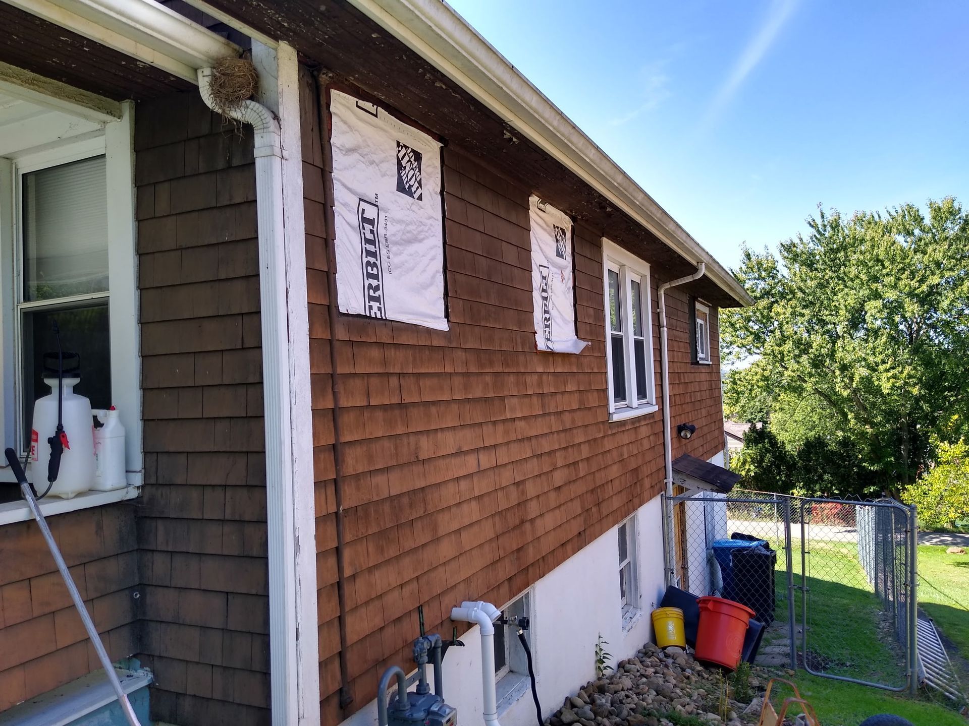 A house with a brown siding and white windows is being remodeled.